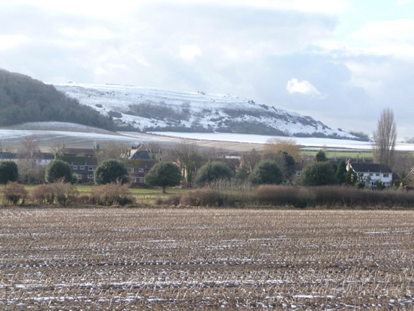 The snow-covered slopes of Hambledon Hill provide a dramatic backdrop to this view of the buildings of Iwerne Courtney village, seen from the A350 which runs parallel to the village's main street. Photo by Chris Downer - for more about Chris Downer click on photo.